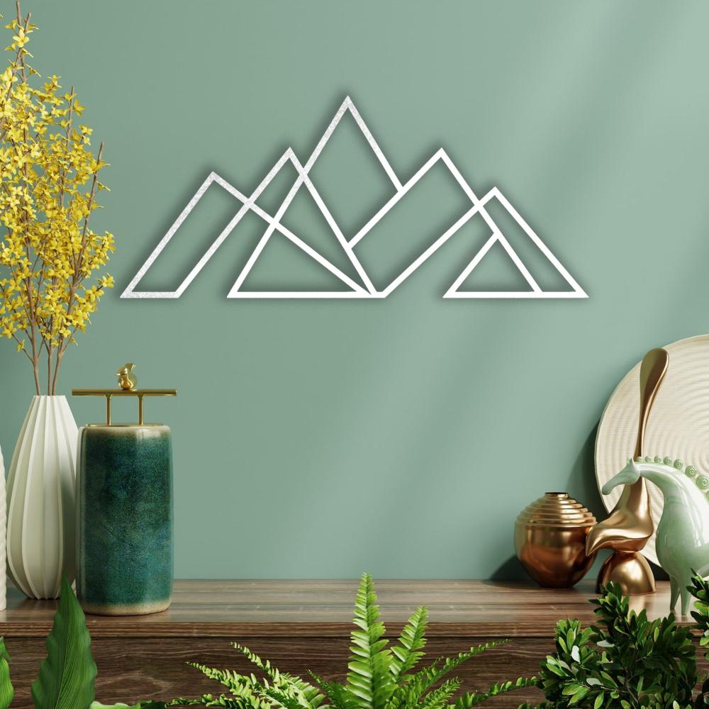 White geometric mountain metal wall art mounted on a green wall, styled with decorative elements and vibrant greenery on a wooden table.