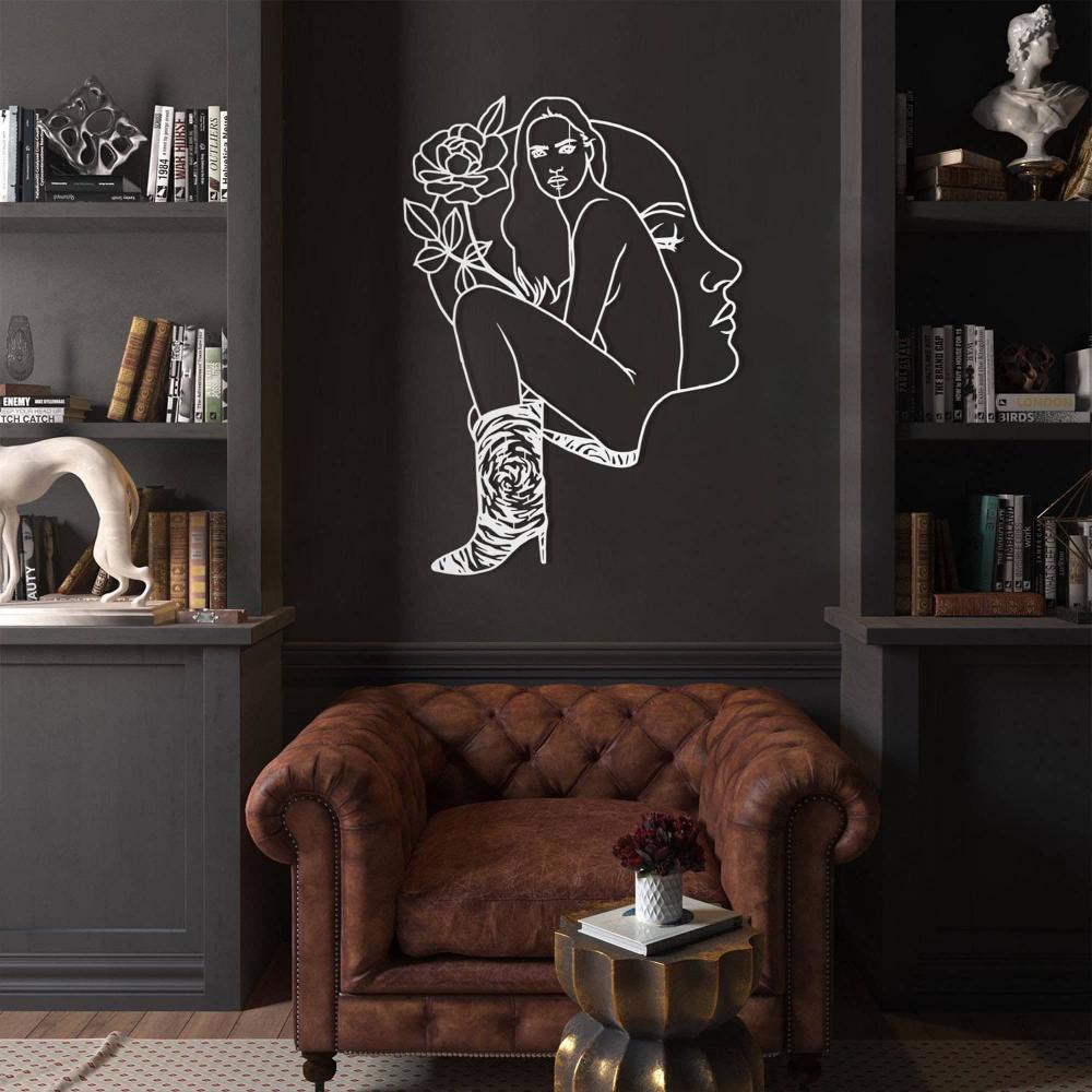 Dark library room with a leather armchair and a white modern metal wall art showcasing a woman's face and body design, adding elegance to the space.