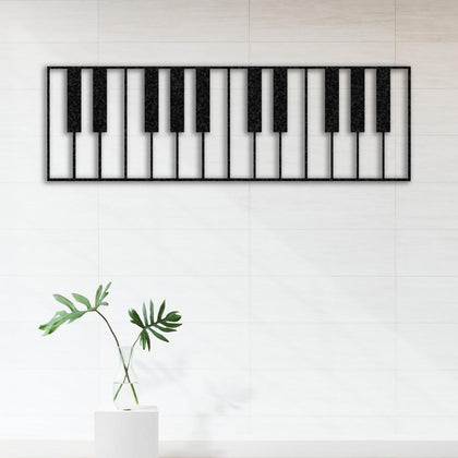 Piano keys-themed metal wall art in a black design, mounted on a tiled white wall. The simple and elegant decor features a single green leaf in a glass vase placed on a white pedestal, creating a minimalist aesthetic.