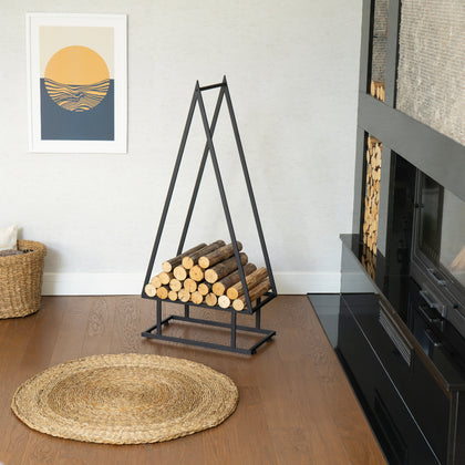 Wooden logs in a metal stand next to a fireplace in a room with a woven mat on the floor. pine tree shaped firewood rack, decorative firewood rack indoor outdoor