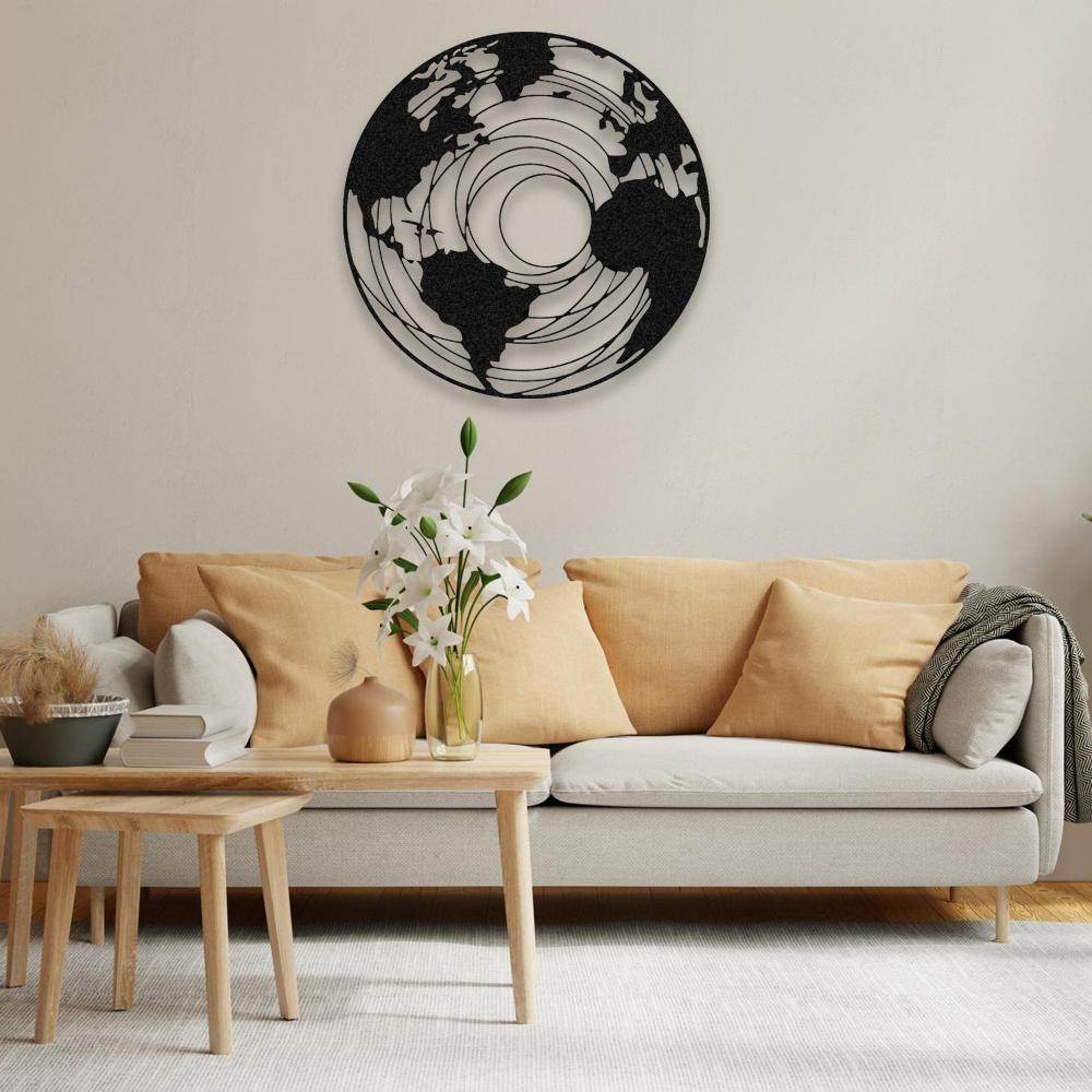 Round earth-themed metal wall art in a white concentric map design, mounted on a dark gray wall above a modern green sofa. The room features wooden flooring, a stylish glass coffee table with decorative elements, and a minimalist aesthetic.