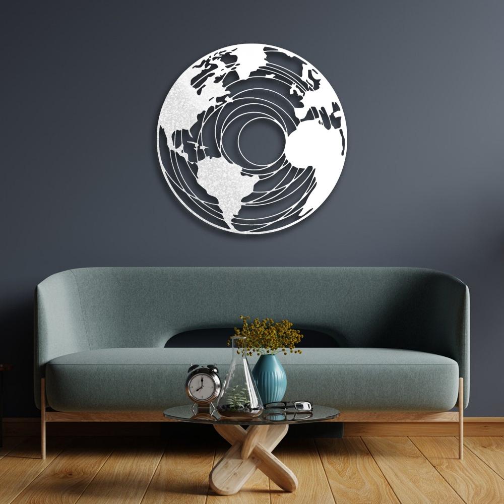 Round earth-themed metal wall art in a white concentric map design, mounted on a dark gray wall above a modern green sofa. The room features wooden flooring, a stylish glass coffee table with decorative elements, and a minimalist aesthetic.