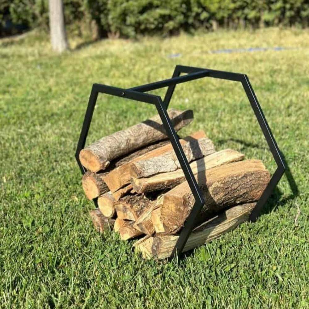 A portable hexagonal-shaped firewood rack made of black metal, placed on a green lawn, filled with wooden logs, highlighting its outdoor usability and sturdy design