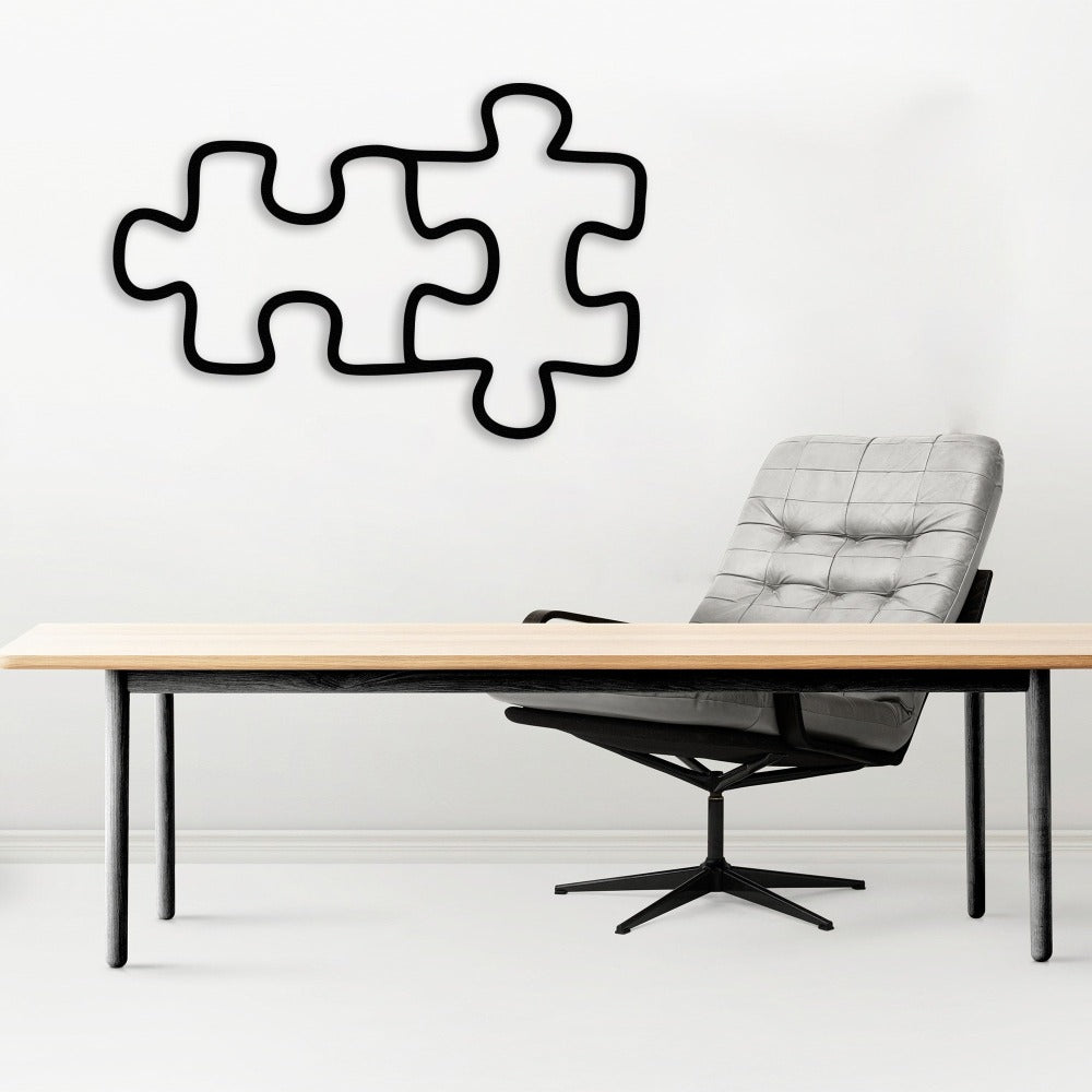Black metal puzzle piece wall decor displayed above a modern office desk with a gray upholstered chair, showcasing a sleek workspace design.