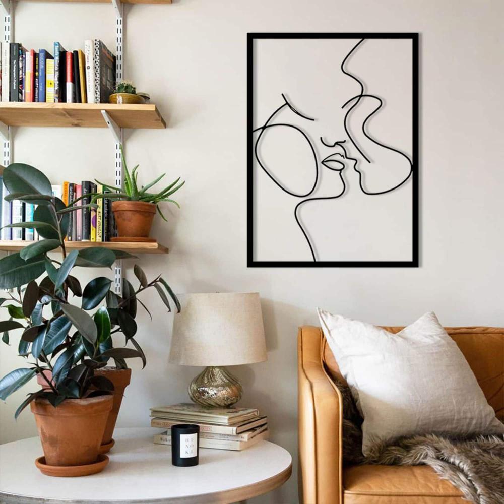 A reading nook featuring a tan leather armchair, potted plants, and a "Relationship Goals" abstract metal wall art of a couple in minimalist lines, adding a romantic touch to the decor.