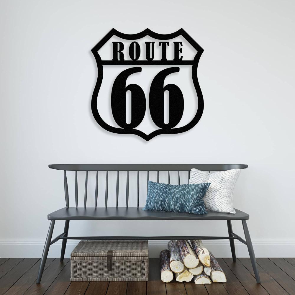 Black metal wall art of the iconic Route 66 sign mounted on a white wall above a modern bench with decorative pillows. Firewood and a woven storage basket are placed underneath, creating a cozy Americana-inspired decor setting.
