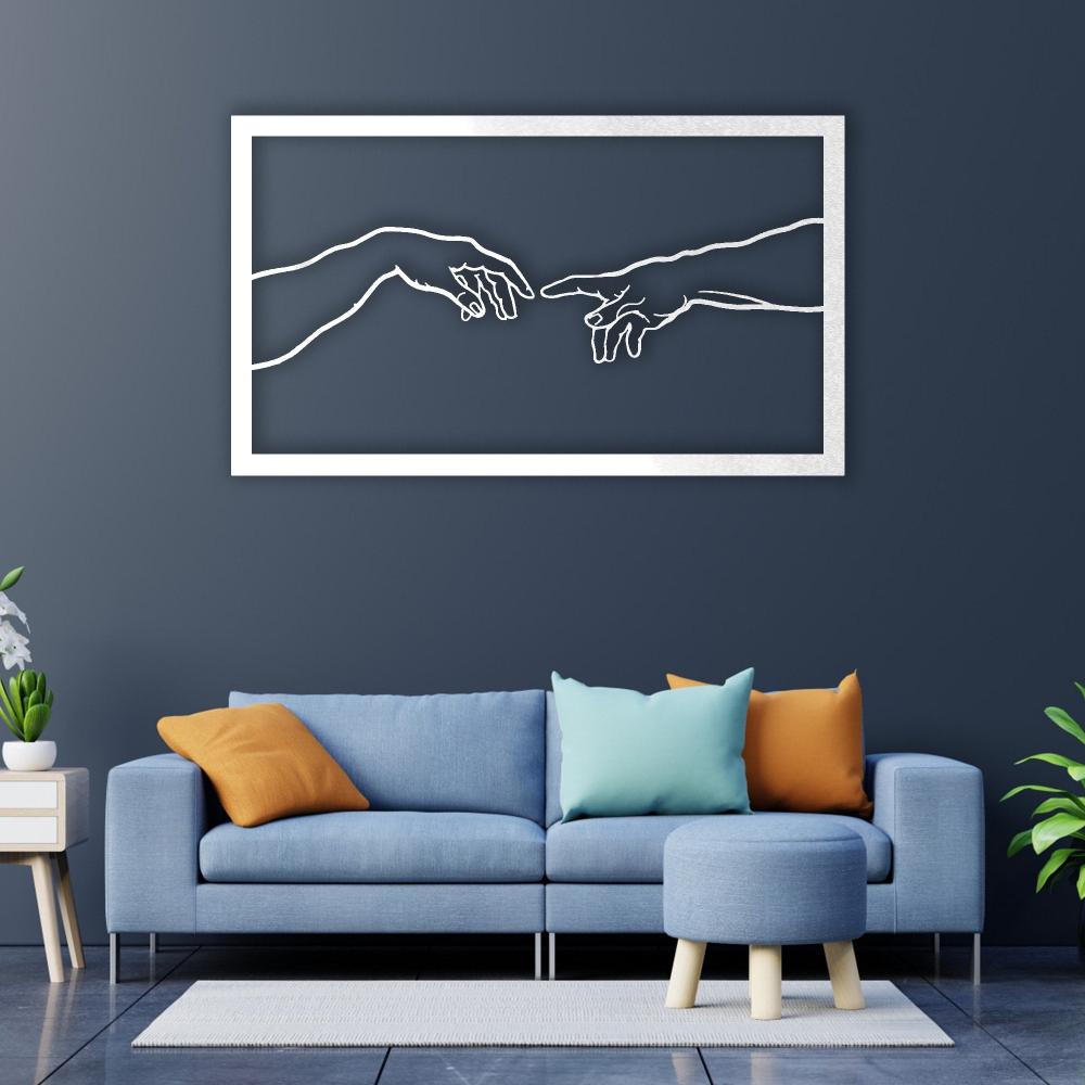 Modern white metal wall art inspired by Michelangelo's "Creation of Adam," featuring two hands reaching toward each other, mounted above a stylish blue sofa with colorful accent pillows, creating a sophisticated and artistic living room ambiance.