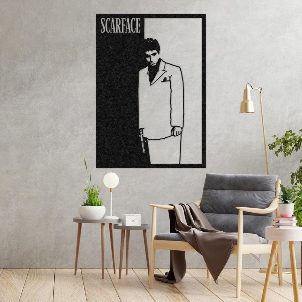 Scarface movie wall art featuring a bold black and white silhouette of a man in a suit with a gun, displayed on a textured gray wall, paired with a cozy wooden armchair draped with a blanket, modern side tables, a table lamp, and greenery for an elegant living space.