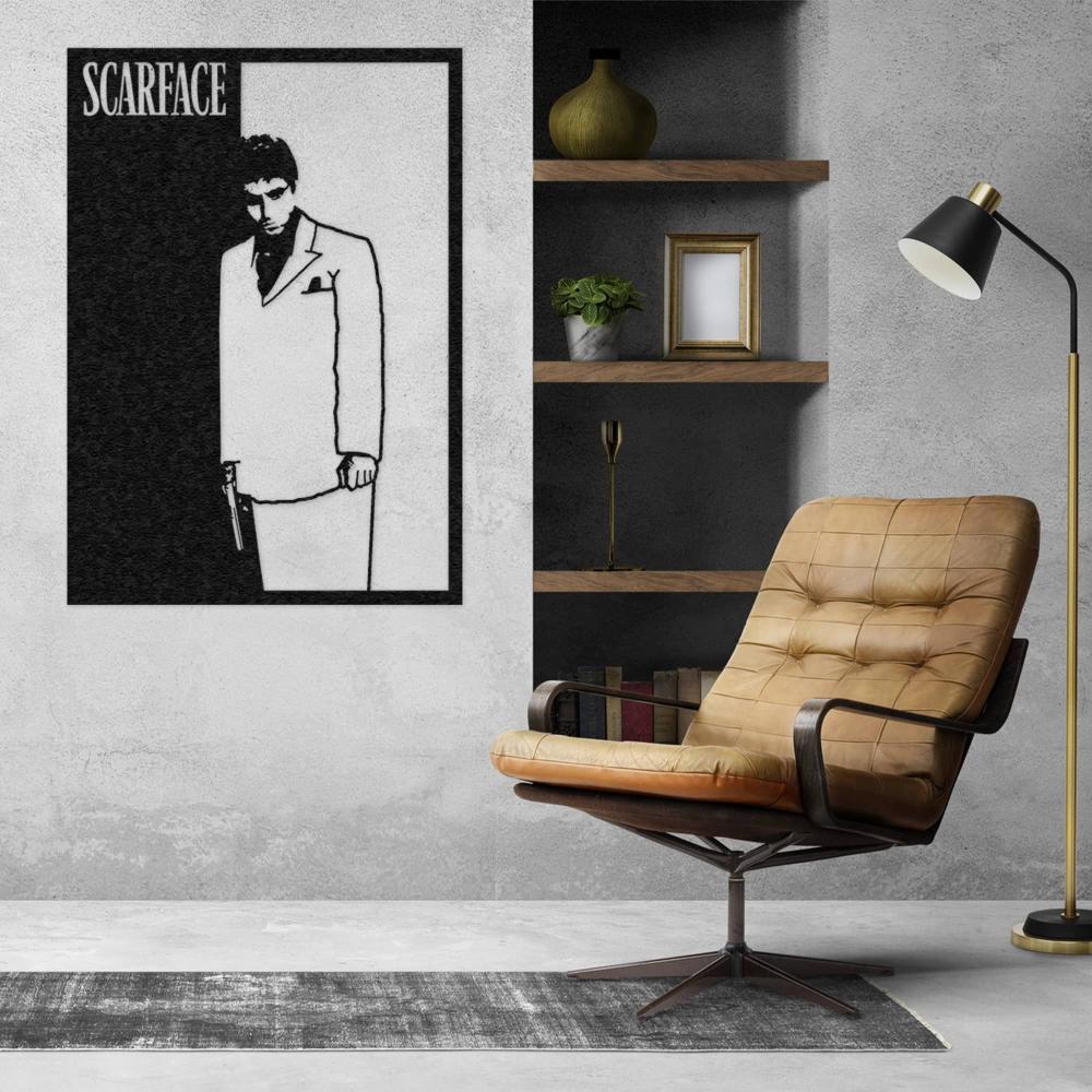 Black and white Scarface wall art featuring a silhouette of a man in a suit holding a gun, displayed on a concrete-textured wall next to a leather armchair and modern shelves with decorative items in a contemporary setting.