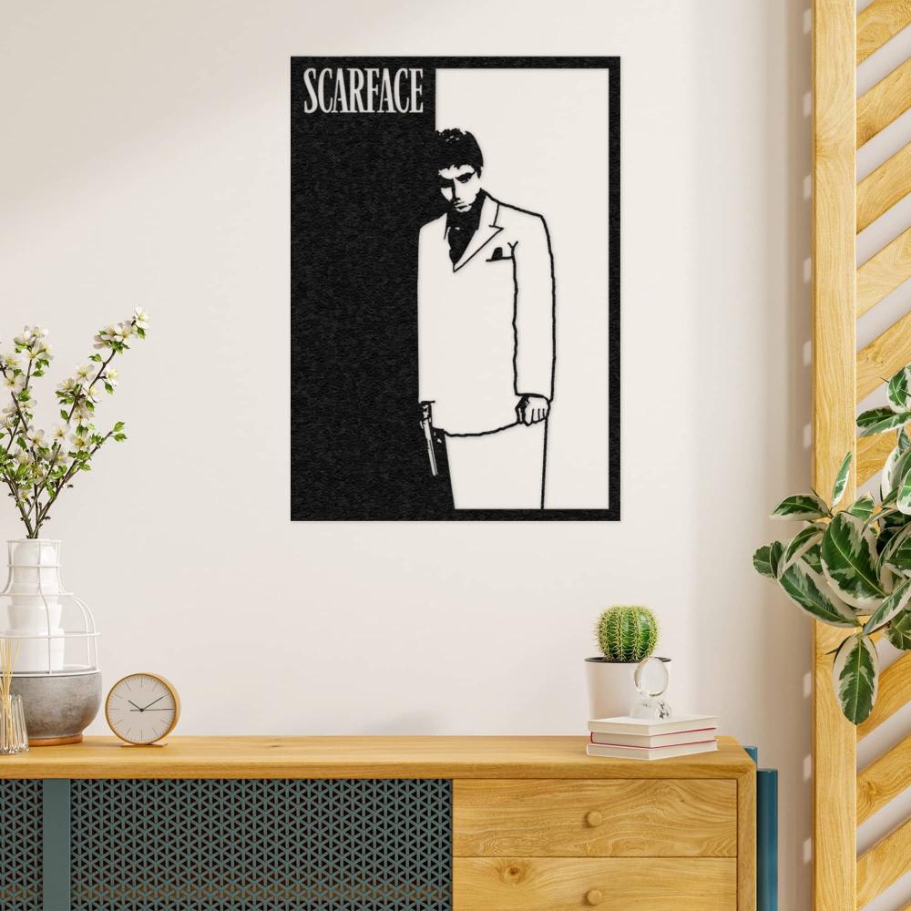 Black and white Scarface wall art featuring a silhouette of a man in a suit holding a gun, displayed on a light cream wall above a modern wooden console with decorative plants and books in a minimalist setting.