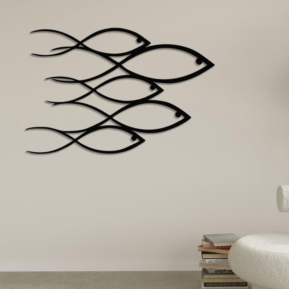 Black metal wall art showcasing a school of fish design mounted on a neutral beige wall in a modern living room, complemented by a stack of books and a minimalist white chair.