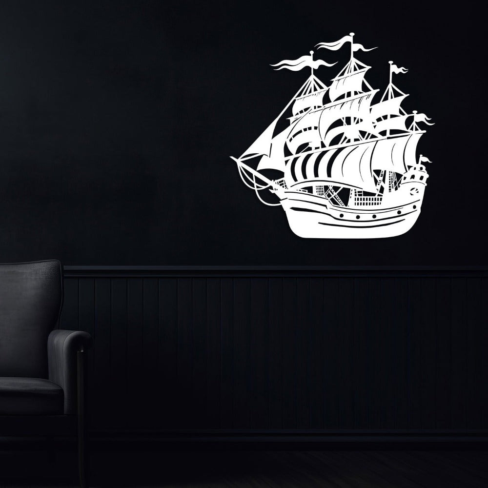 White metal ship wall art showcasing an intricately designed sailing vessel with masts and flags, mounted on a dark black wall in a sophisticated setting with a modern black armchair.
