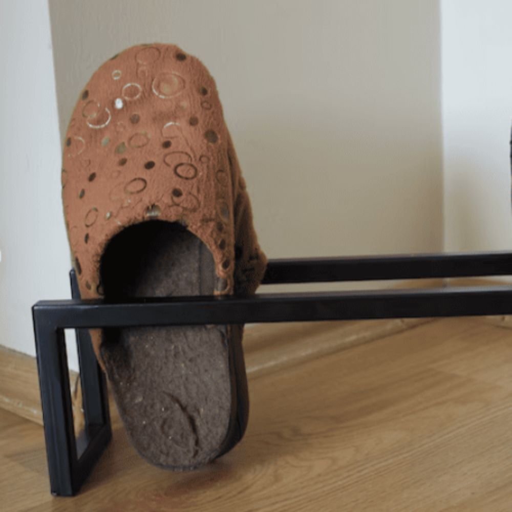 A single pair of brown slippers placed on a minimalist black metal shelf, captured on a wooden floor
