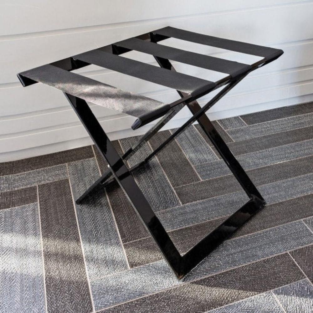 A sleek black foldable luggage rack with metallic finish placed on a modern patterned tile floor, enhancing its aesthetic appeal.