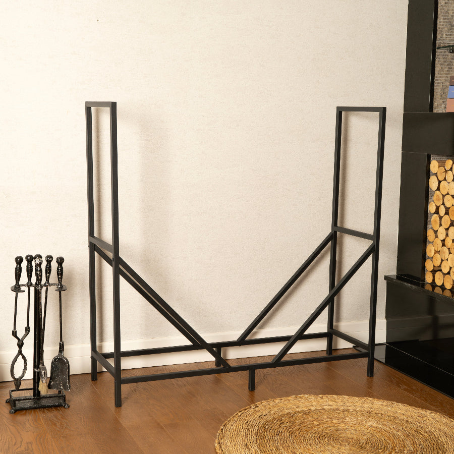Black metal firewood rack against a white wall with fireplace tools and stacked logs.