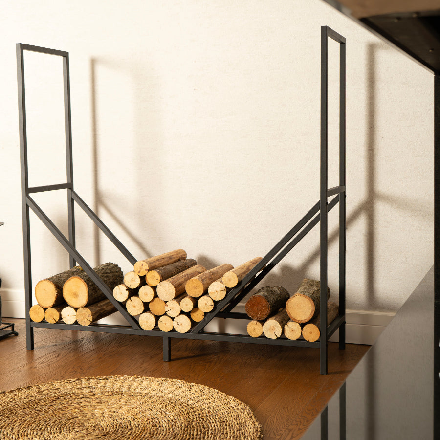 Black metal firewood rack with logs against a white wall.