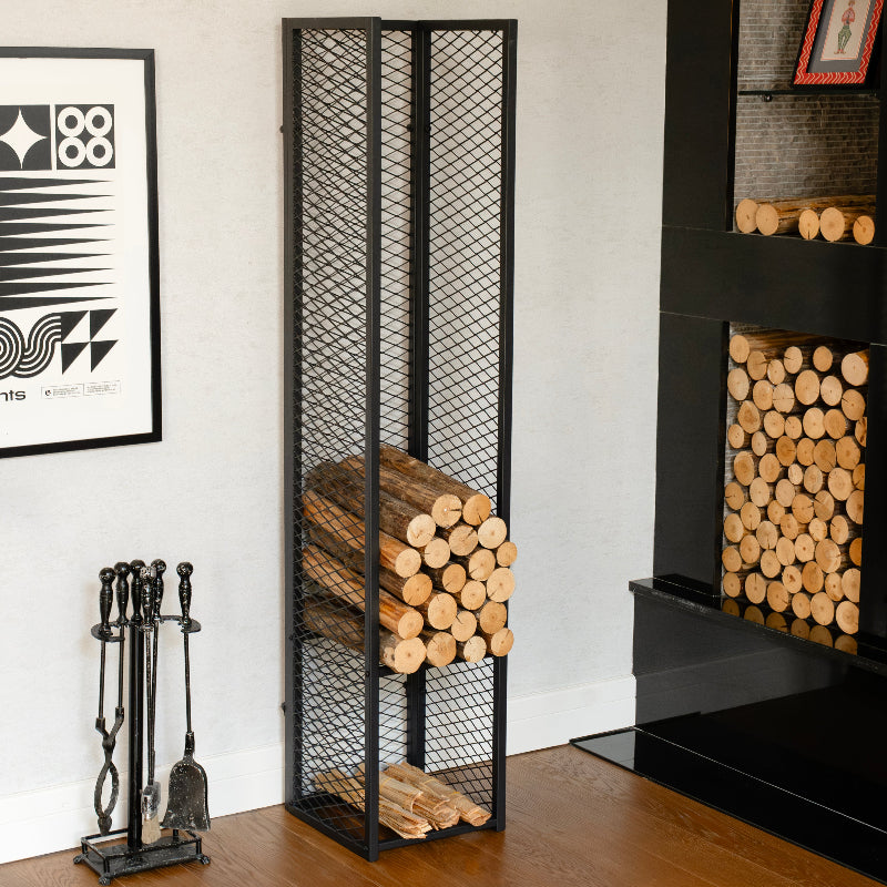 Black metal firewood storage rack with logs next to a fireplace.