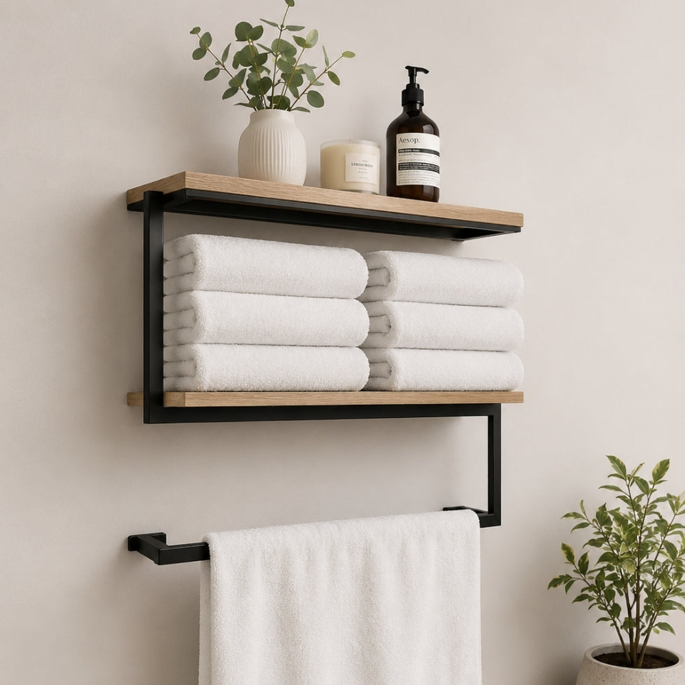 Black wall mounted 2-tier towel shelf with towel bar holding folded towels, plant, bottle, and hanging towel.