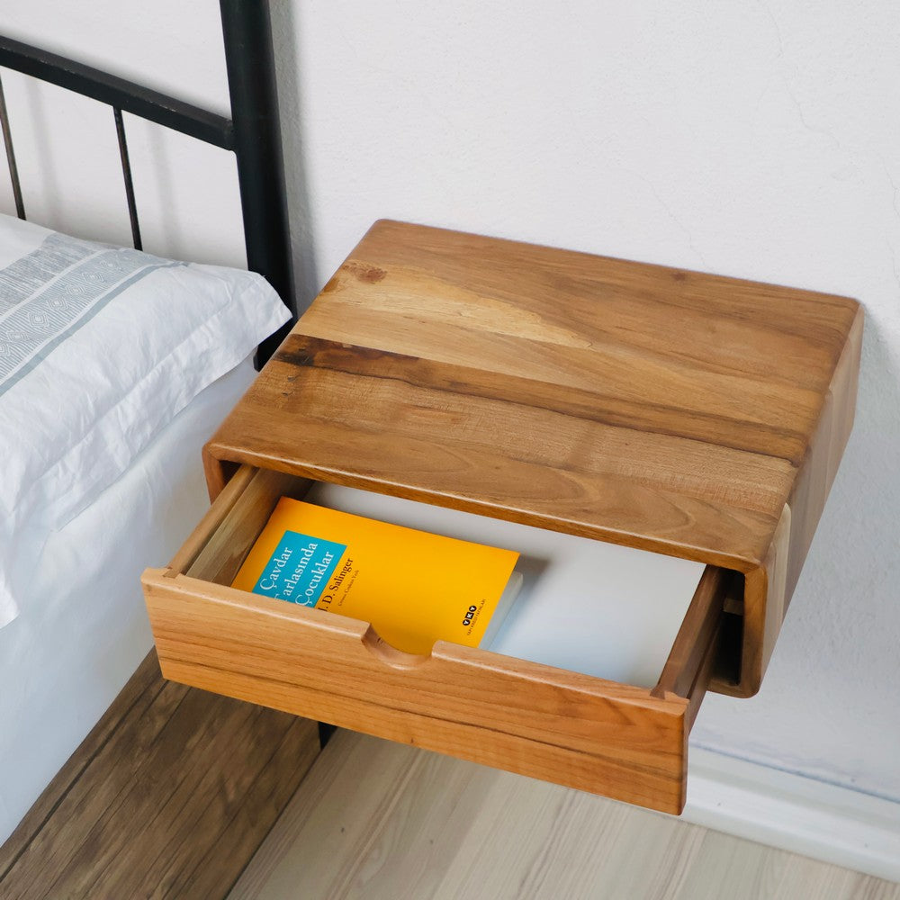 Wall-mounted wooden bedside table with its pull-out drawer open, revealing a book inside. The natural wood grain finish and compact design make it ideal for minimalist bedroom setups.