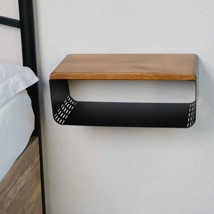 Minimalist wall-mounted wooden and black metal bedside table with a natural wood top and a perforated black metal base. The sleek and functional design is shown for modern bedroom spaces.