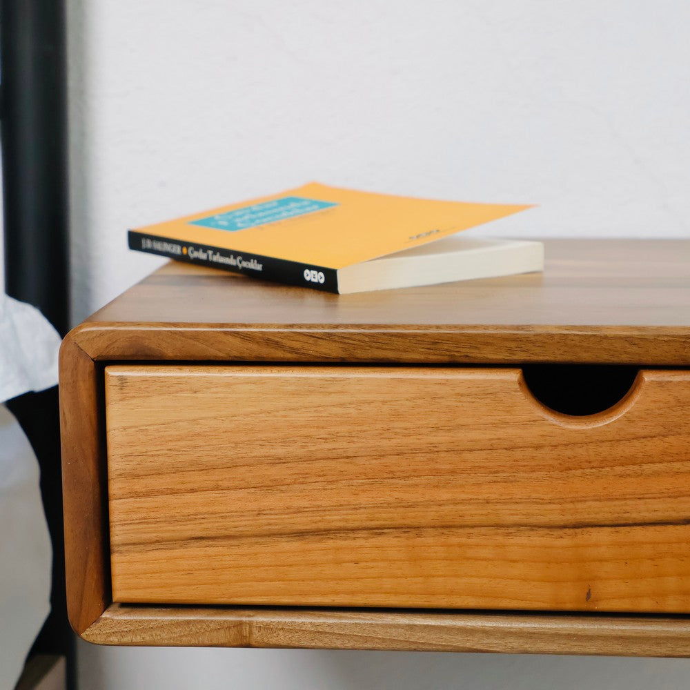 Close-up of a walnut wall-mounted wooden bedside table featuring a natural wood grain finish and a single pull-out drawer. A book is placed on the tabletop, showcasing its functional and stylish design.
