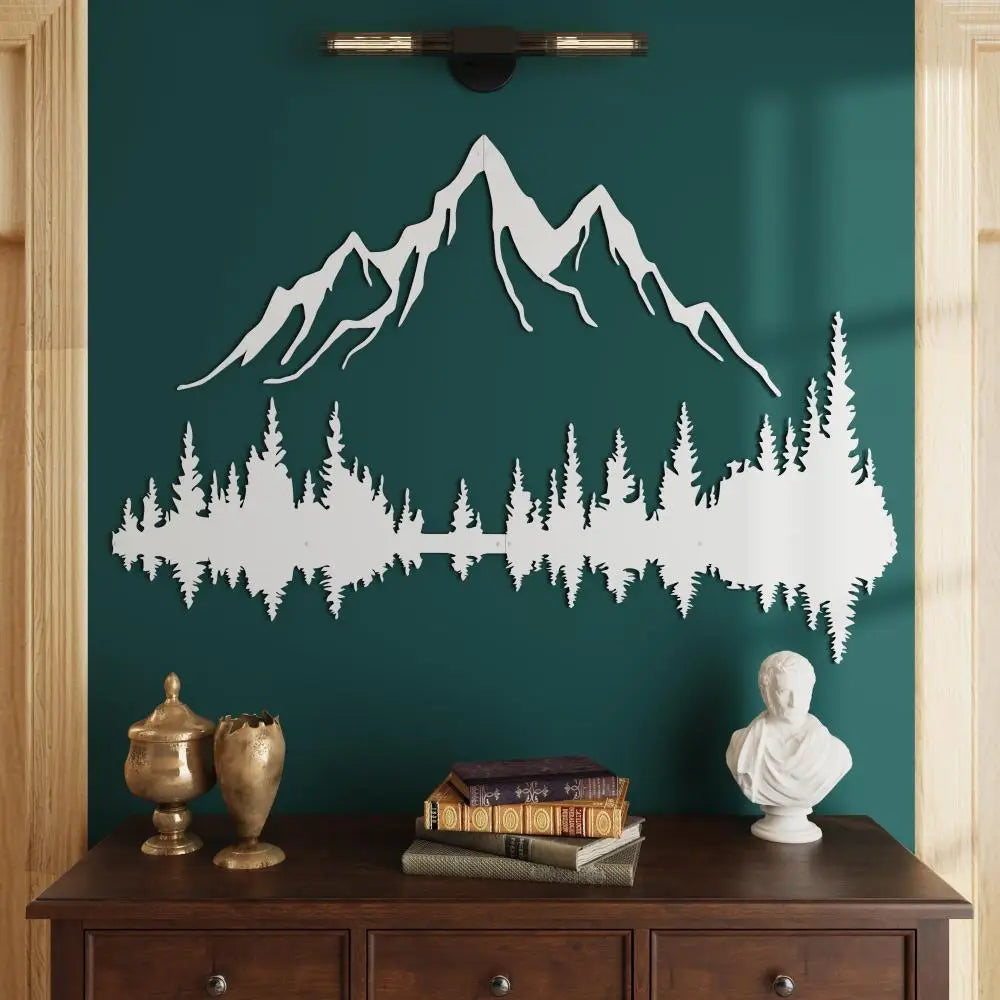 Elegant white mountain and forest metal wall art mounted on a rich green wall, complemented by a dark wooden console table adorned with antique gold decor pieces, stacked books, and a classical white bust.