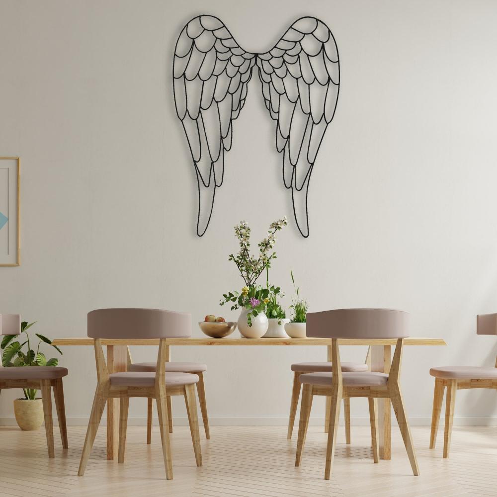 Black metal angel wings wall art mounted above a wooden dining table with soft beige chairs, decorated with vases of flowers and minimalist decor in a bright dining space.