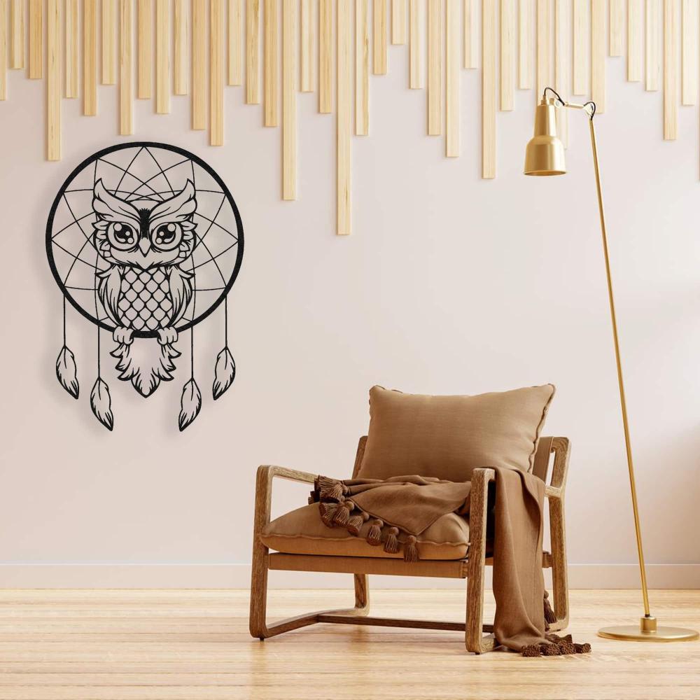 Wise owl dreamcatcher black metal wall art mounted on a light wall, paired with a wooden chair and golden floor lamp, creating a cozy decor.