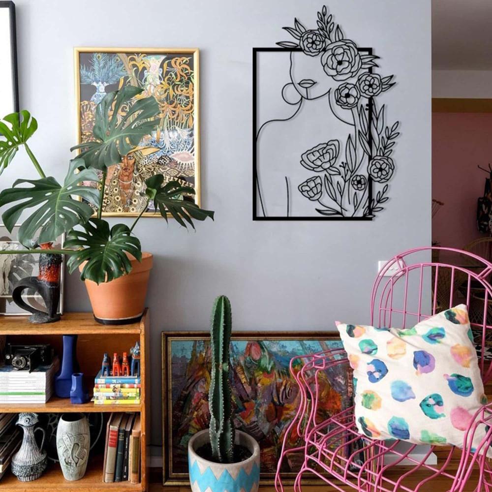 A vibrant living room setup featuring a wall adorned with a metal art piece of a woman's silhouette surrounded by roses, complementing the eclectic decor of plants, colorful artwork, and a pink wire chair.