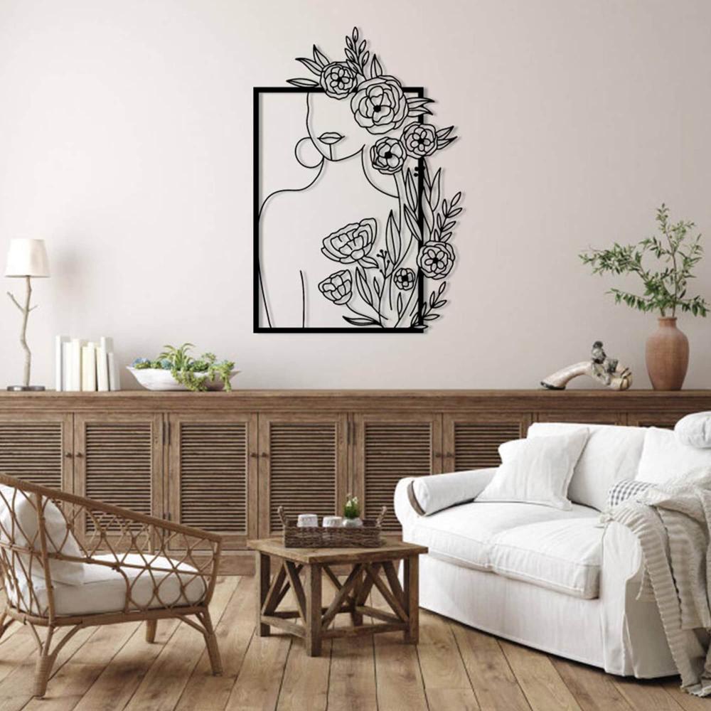 A rustic living room featuring a metal wall art piece depicting a minimalist woman’s silhouette adorned with roses and leaves, mounted above a wooden sideboard with wicker and ceramic decor, enhancing the warm, natural ambiance.
