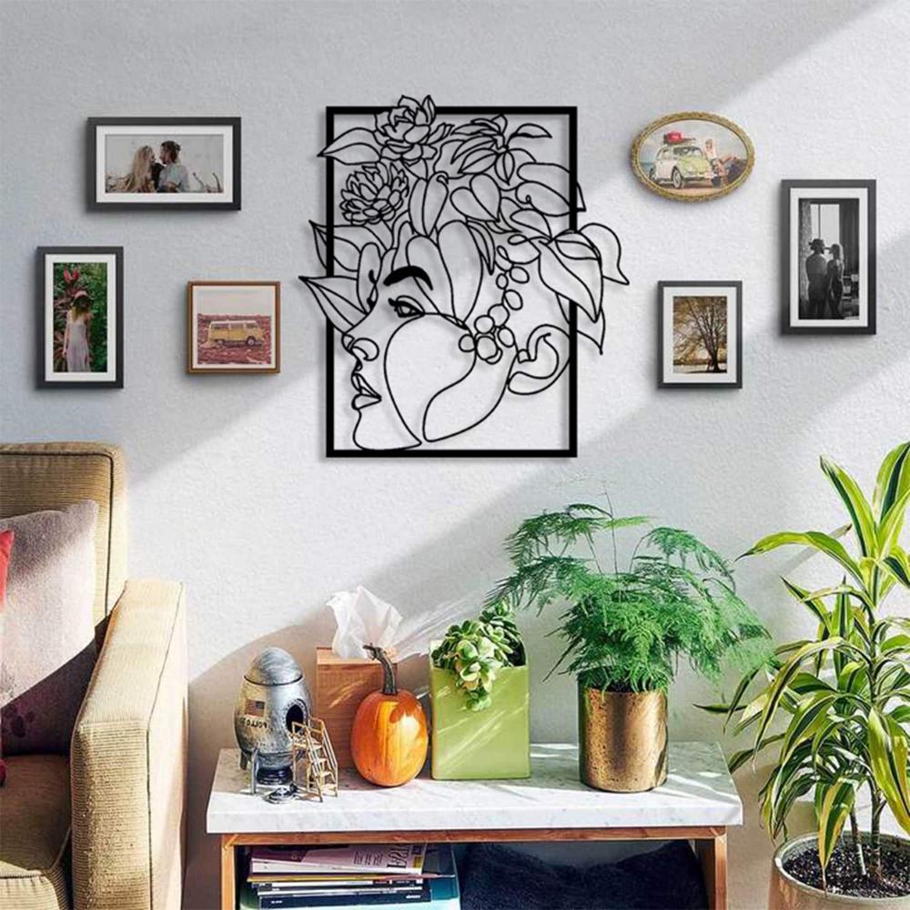 Metal wall art featuring a woman's face with floral patterns, styled as part of a gallery wall in a modern living room with plants and framed pictures.