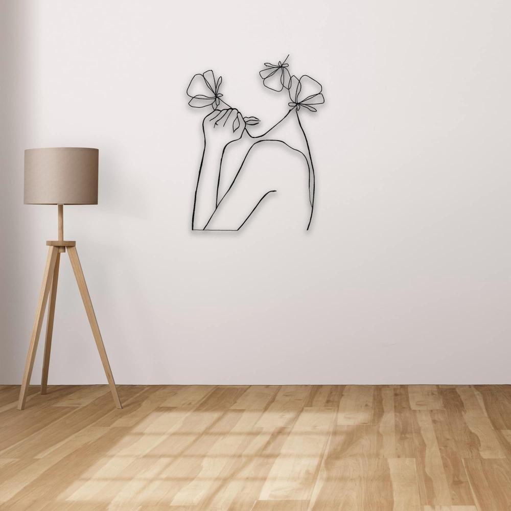 Minimalist line art of a woman with flowers, mounted on a plain wall with a wooden tripod lamp beside it, highlighting the simplicity of the decor.