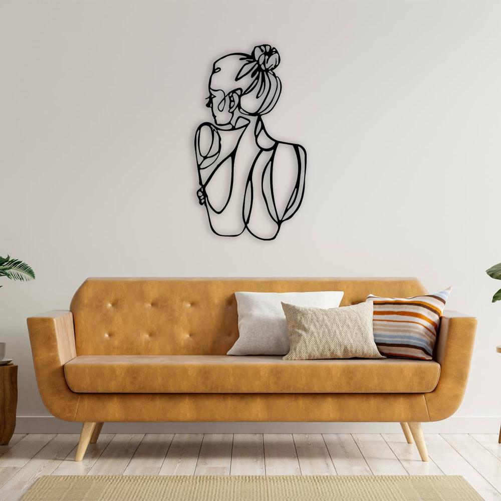 A contemporary living room featuring a black metal wall art of a woman’s figure, hung above a mustard yellow sofa with layered cushions.