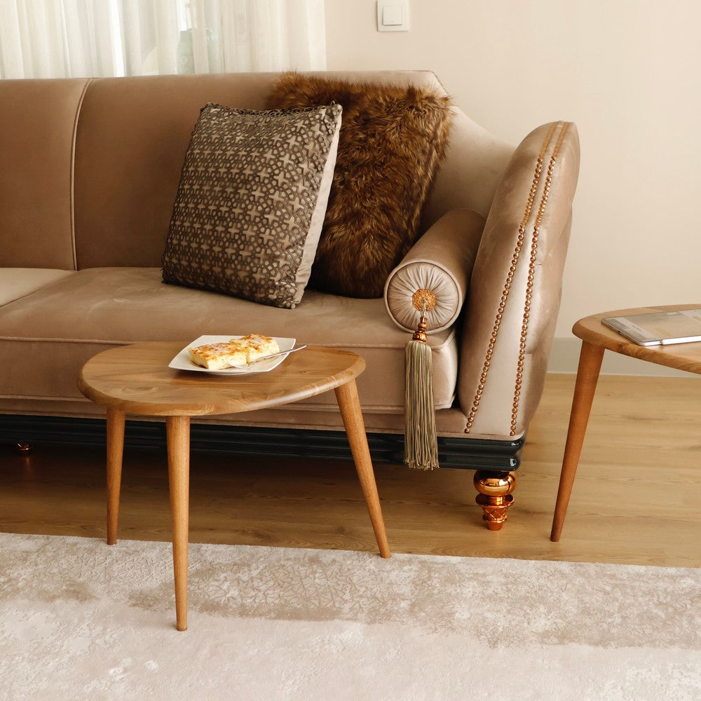 Small wooden nesting table with a plate of pastries, styled in a warm and inviting living room beside a beige sofa and furry pillows.
