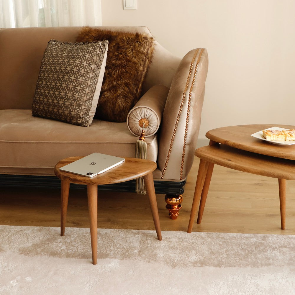 Small wooden nesting table with a tablet on top, placed beside a beige sofa and furry pillows in a cozy living room setting.