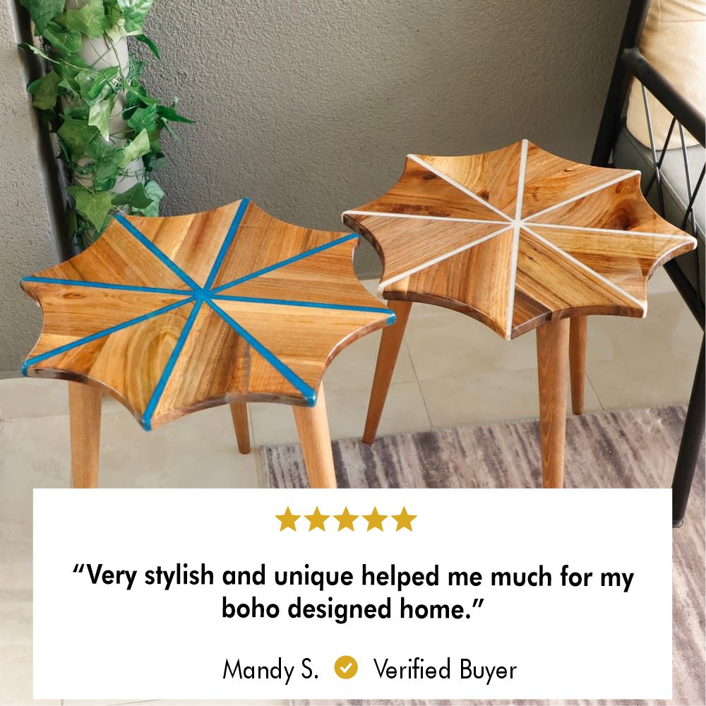 Pair of star-shaped wooden side tables, one with a blue inlay and the other with a white inlay, displayed on a textured rug next to green decorative plants.