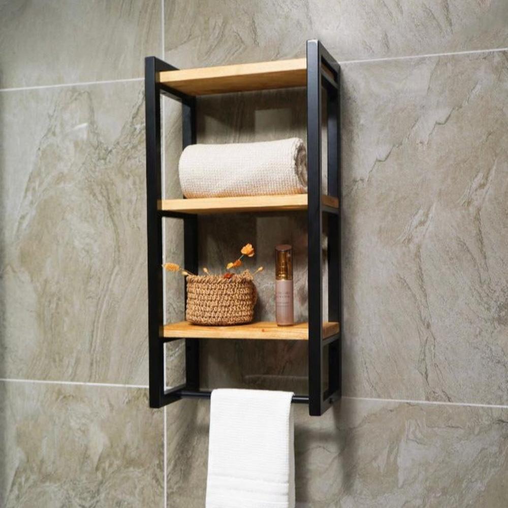 Three-shelf bath towel holder mounted on a stone wall, featuring black metal frames, wooden shelves, and displaying a rolled towel, decorative items, and a hanging towel.