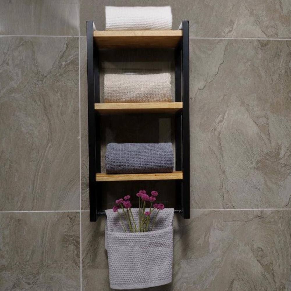 Three-shelf bath towel holder mounted on a stone-textured wall. The organizer features a black metal frame with wooden shelves, displaying folded beige and gray towels.