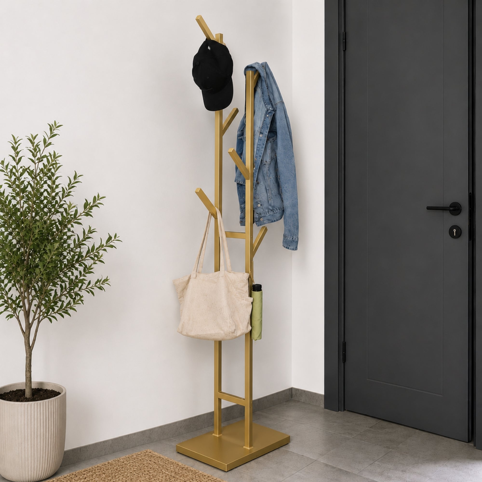 Gold freestanding 6-hook metal coat rack with jacket, cap, tote bag, and umbrella beside a dark entryway door.