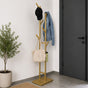 Gold freestanding 6-hook metal coat rack with jacket, cap, tote bag, and umbrella beside a dark entryway door.