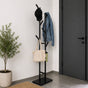 Modern black freestanding 6-hook metal coat rack holding a cap, jacket, tote, and umbrella near an entryway door.