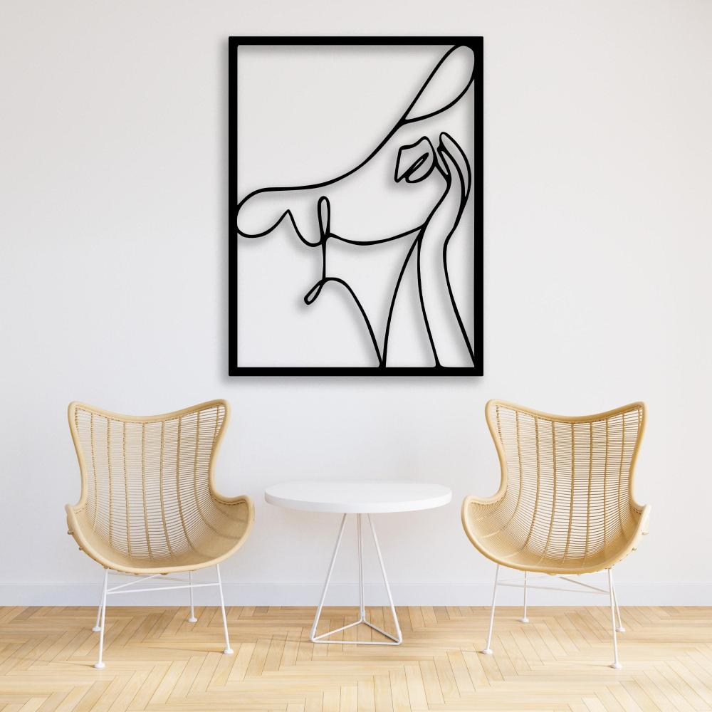 Abstract woman with a hat black metal wall art showcased on a white wall between two wicker chairs with a small round table.