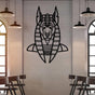 Black metal wall art of Anubis, the ancient Egyptian god, featuring a detailed geometric design, mounted on a light brick wall in a modern bar setting. Industrial-style pendant lights and arched windows frame the space, with wooden chairs arranged below.