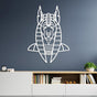 White metal wall art of Anubis, the ancient Egyptian god, featuring a clean geometric design, mounted on a dark gray wall above a modern white cabinet with open shelves. The cabinet holds neatly arranged books and decorative items, including a small clock and a green plant.
