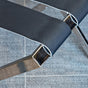 Close-up view of a grey leather strap on a satin nickel metal luggage rack, showing the powder-coated frame and matching strap finish.
