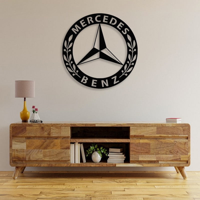 A sophisticated black Mercedes-Benz-inspired metal car logo wall art displayed above a rustic wooden console table adorned with books, a small plant, and a yellow lamp, creating a refined and timeless decor.