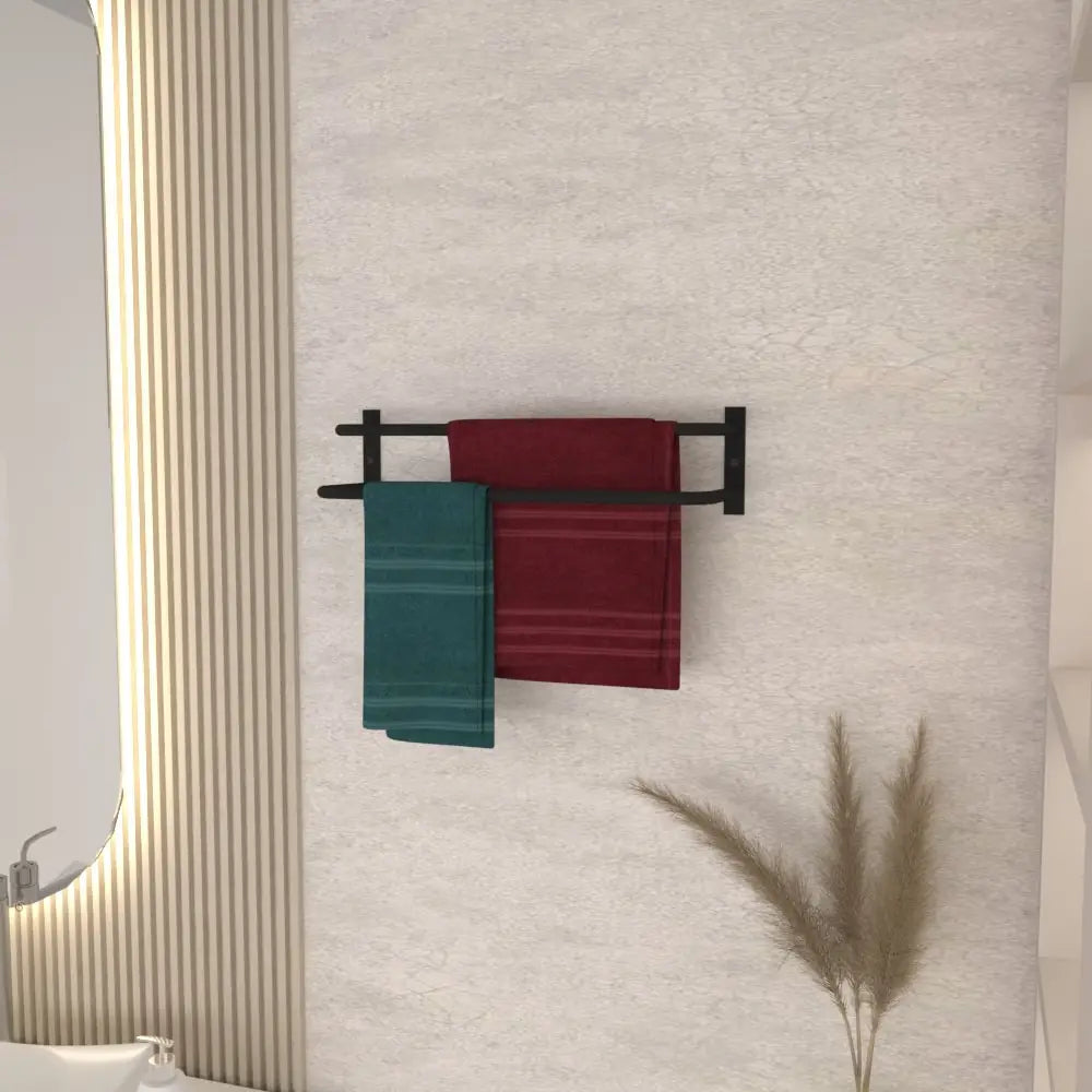 A wall-mounted black towel holder holding a burgundy and teal towel, styled in a modern bathroom with a beige wall, open shelving featuring decorative items, and a vase of pampas grass for a natural touch.