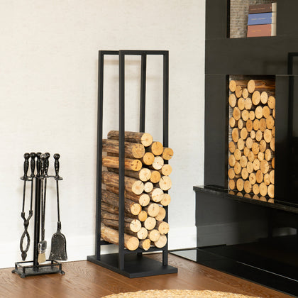 Elevated Black Metal Firewood Rack with logs next to a fireplace and fire tools on a wooden floor