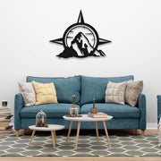 Compass and mountain metal wall art displayed above a blue sofa in a cozy living room with layered coffee tables and books.