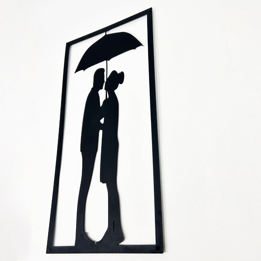 Close-up angled view of a black metal wall art featuring a couple under an umbrella, showing the laser-cut design detail.